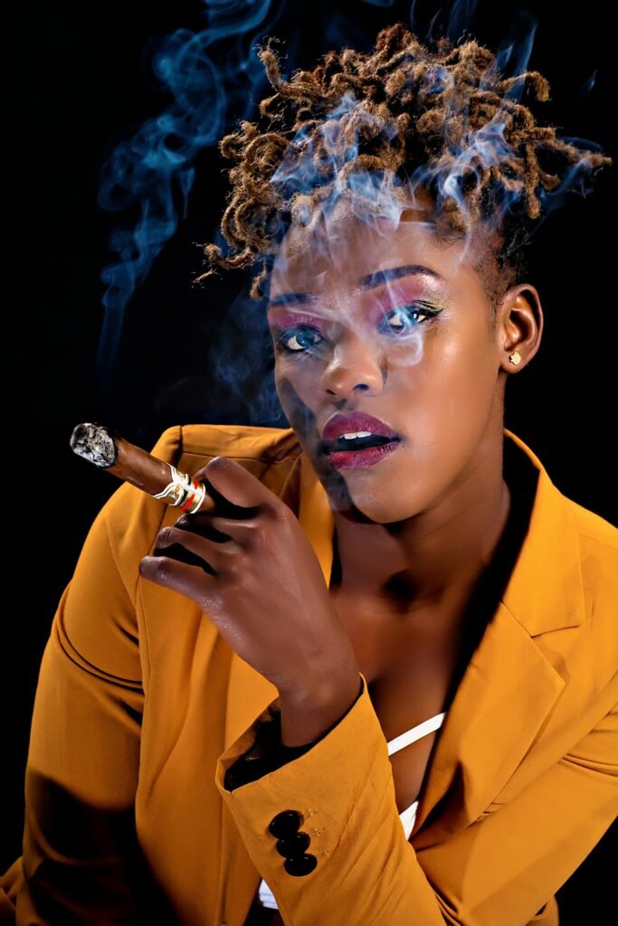 Confident woman with dreadlocks smoking a cigar in a bold outfit, exuding style and sophistication.